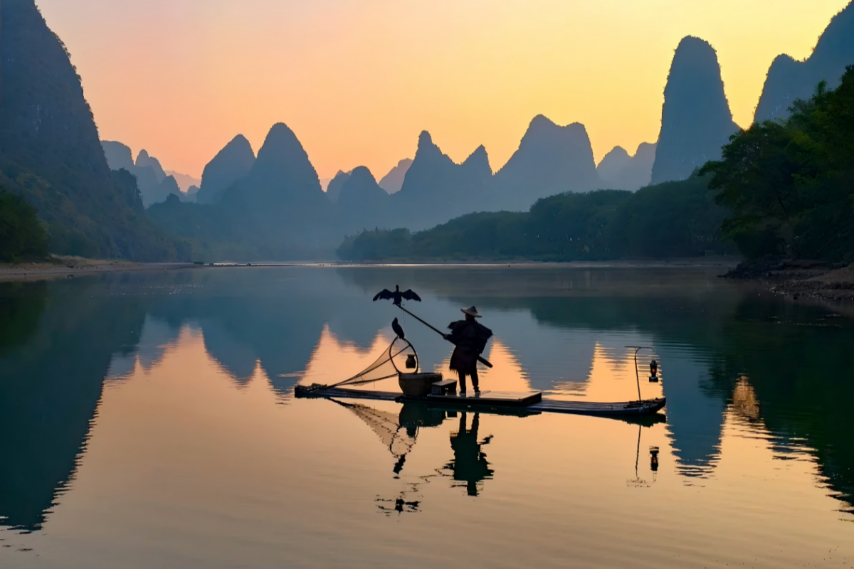 Silhouette of a fisherman on a small bamboo raft with a bird perched on a pole, gliding on a glassy river with karst mountains reflected in the water at sunrise.