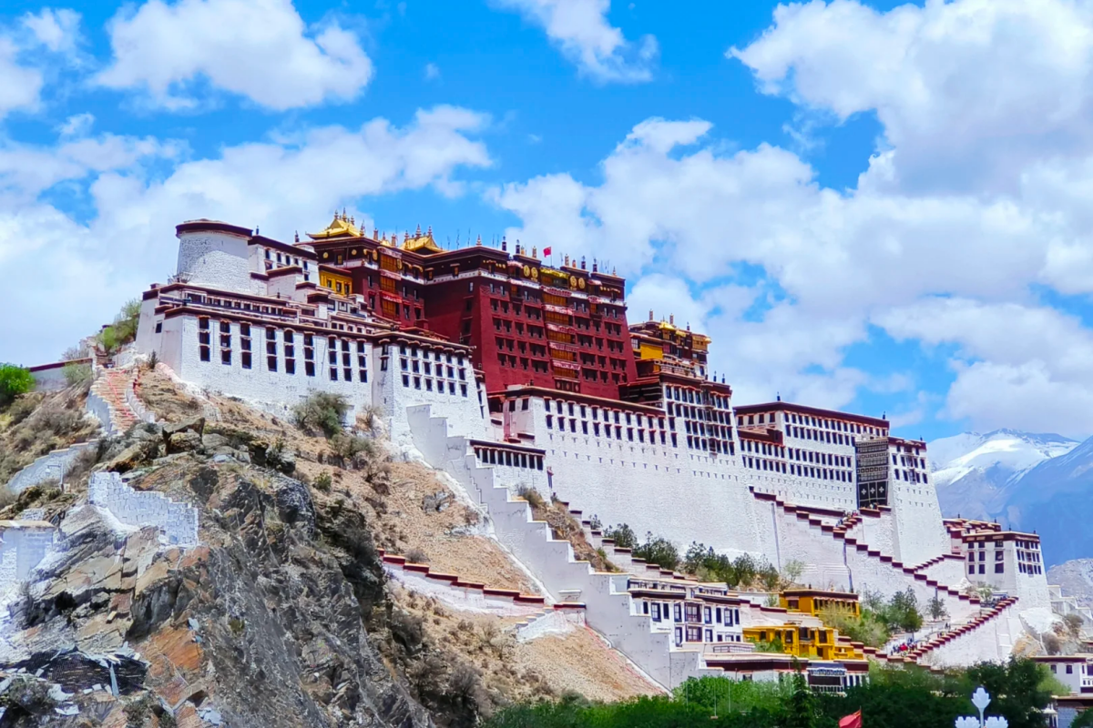 The Potala Palace complex with white walls and red buildings under a bright blue sky.