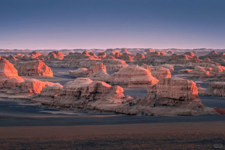Wide view of a barren desert landscape filled with rounded rock formations glowing orange in low sunlight under a clear sky.