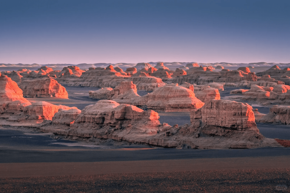 Wide view of a barren desert landscape filled with rounded rock formations glowing orange in low sunlight under a clear sky.