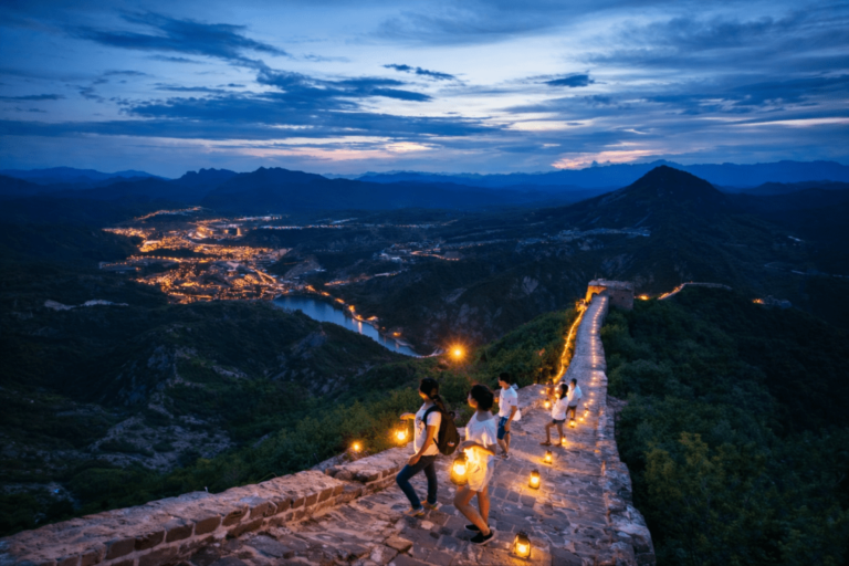Visitors walking along the Great Wall at dusk with lantern lights and a valley town glowing below