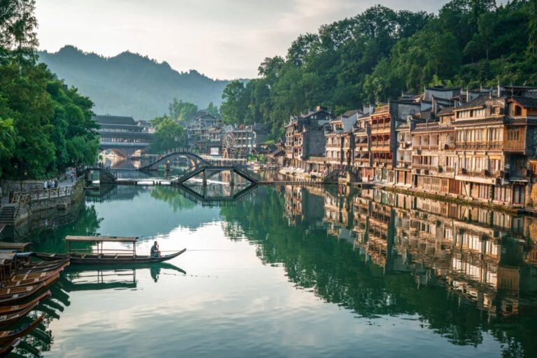 Traditional riverside houses and arched bridges reflected in calm water in Fenghuang Ancient Town.