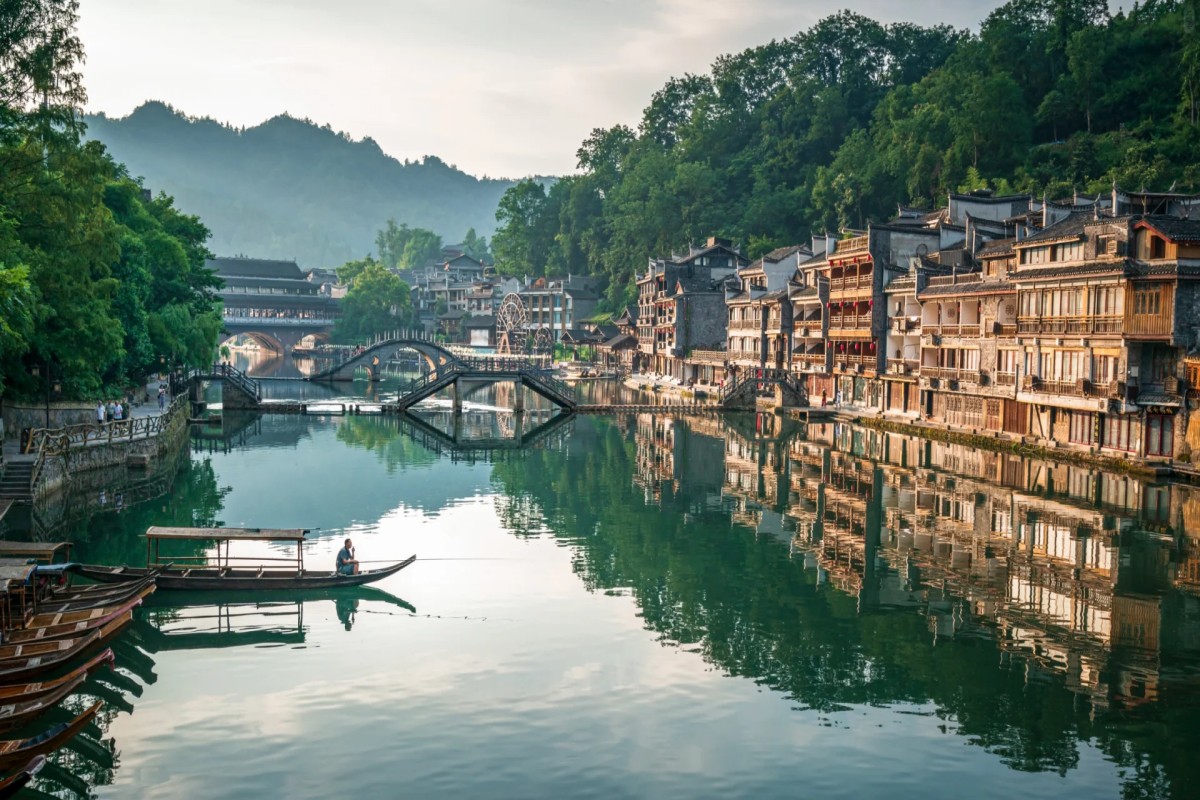 Traditional riverside houses and arched bridges reflected in calm water in Fenghuang Ancient Town.