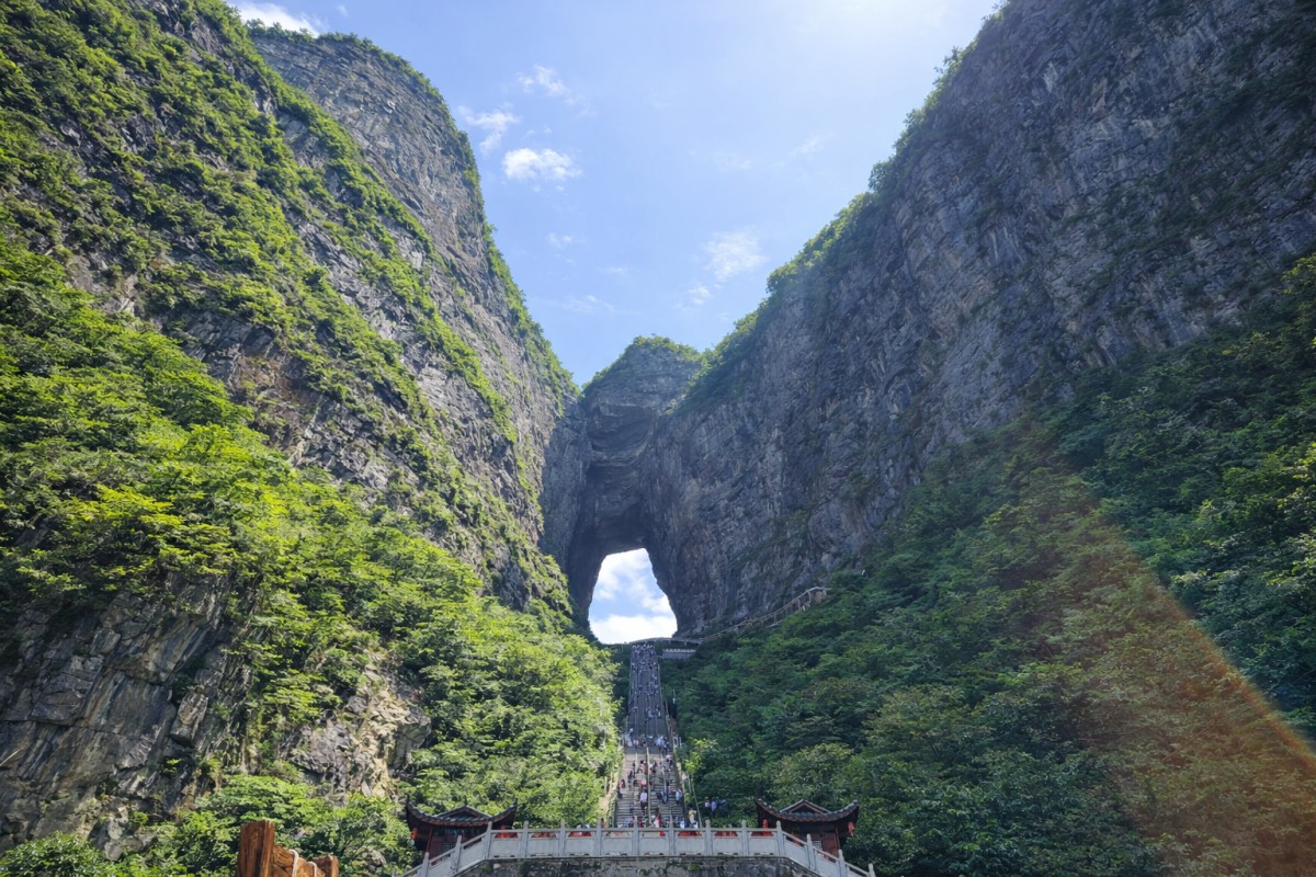 Steep staircase leading through Tianmen Cave, a massive natural rock arch surrounded by green cliffs.
