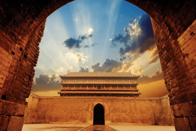 View of the ancient Xi’an City Wall and gate framed by a stone arch at sunset, with dramatic clouds and golden light.