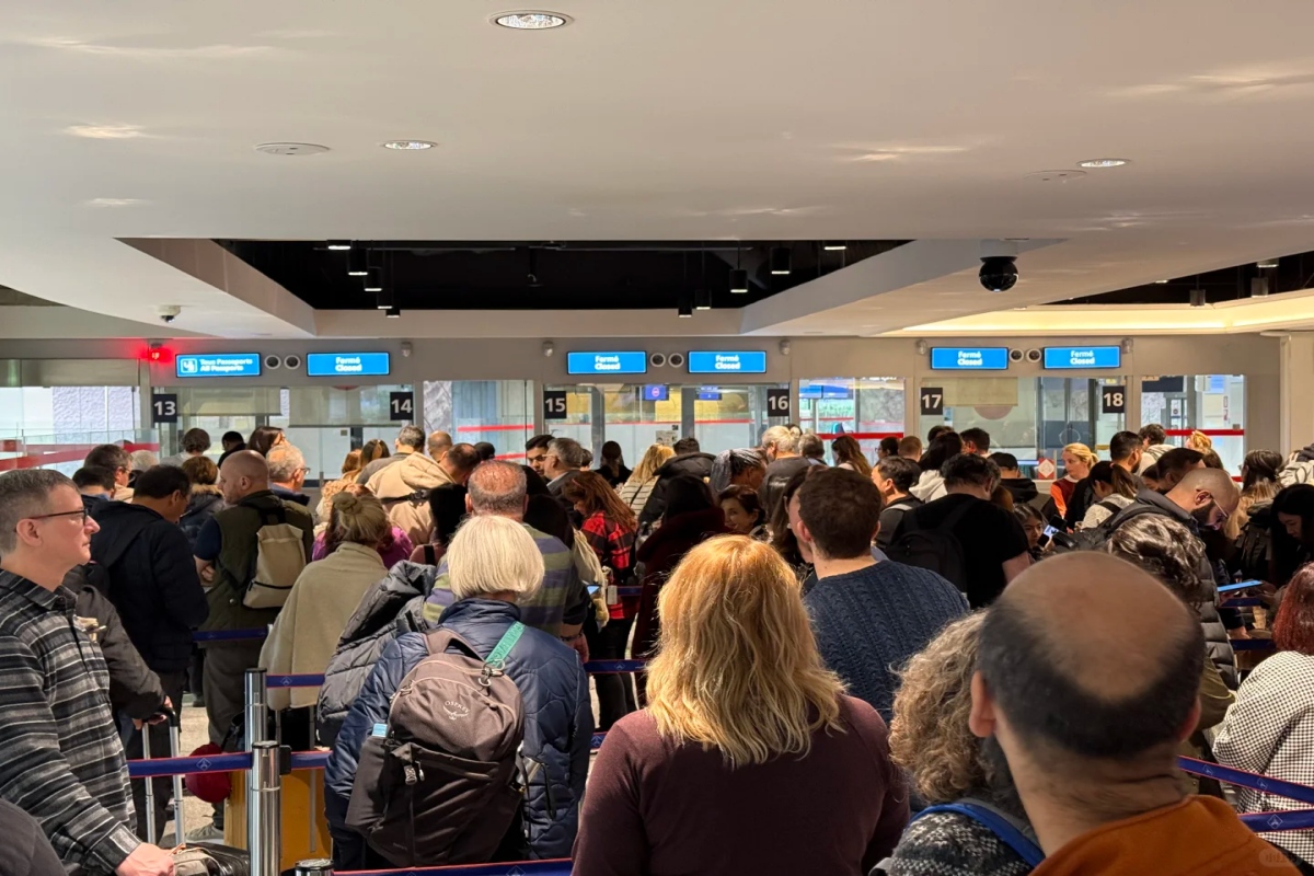 Crowded queue of travelers waiting at airport passport control counters.
