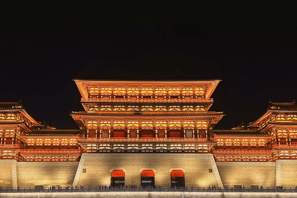A brightly illuminated traditional Chinese building complex at night, showcasing intricate architecture and warm lighting.