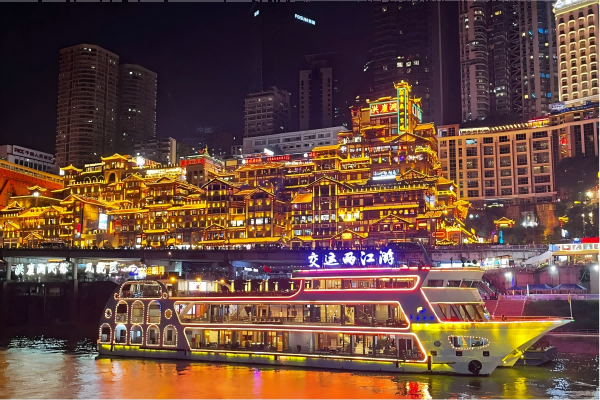 Illuminated traditional-style buildings under a red bridge in Chongqing at night.