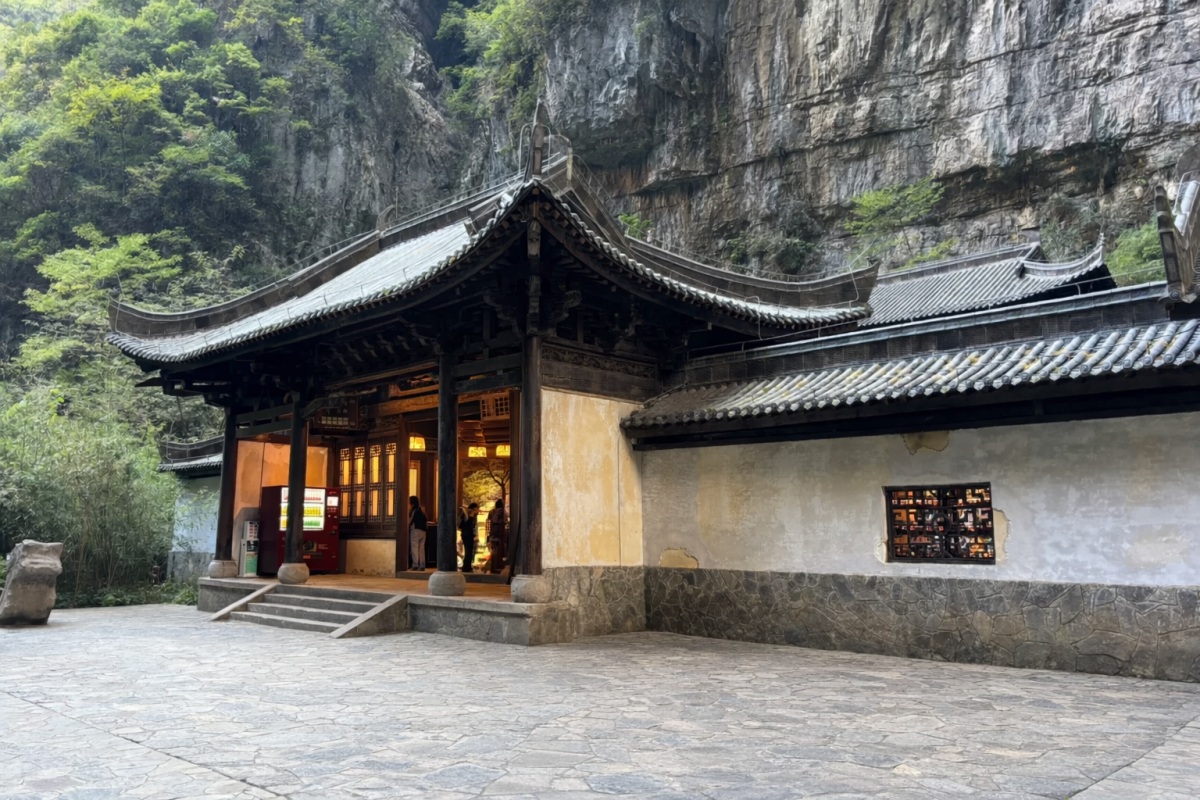 Traditional temple built against a rocky cliff in a forested mountain area.
