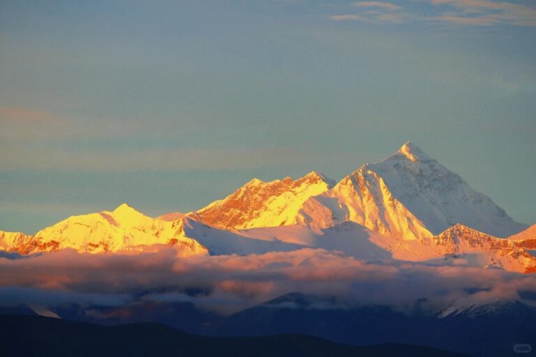 Sunrise lighting Mount Everest and nearby Himalayan peaks above clouds.