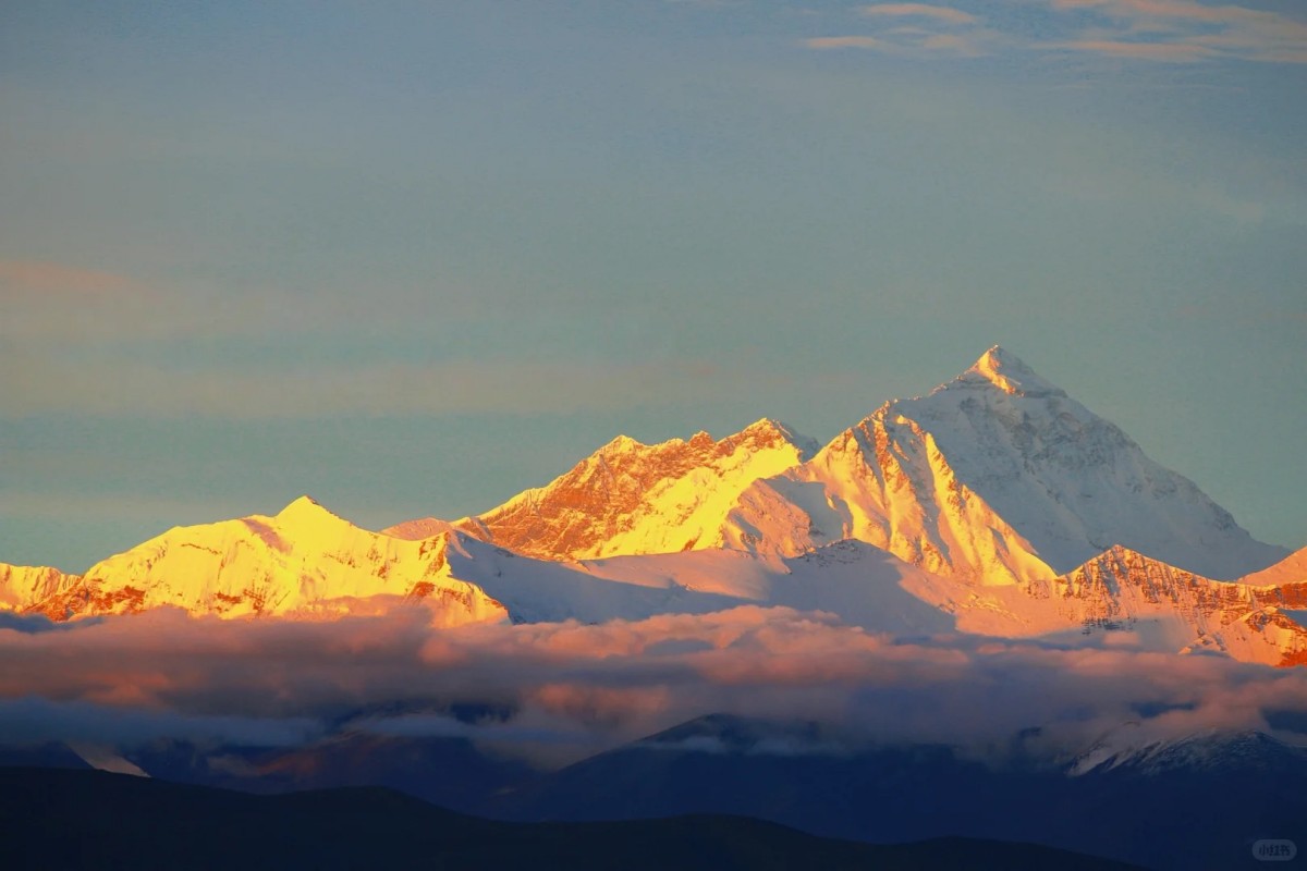 Sunrise lighting Mount Everest and nearby Himalayan peaks above clouds.
