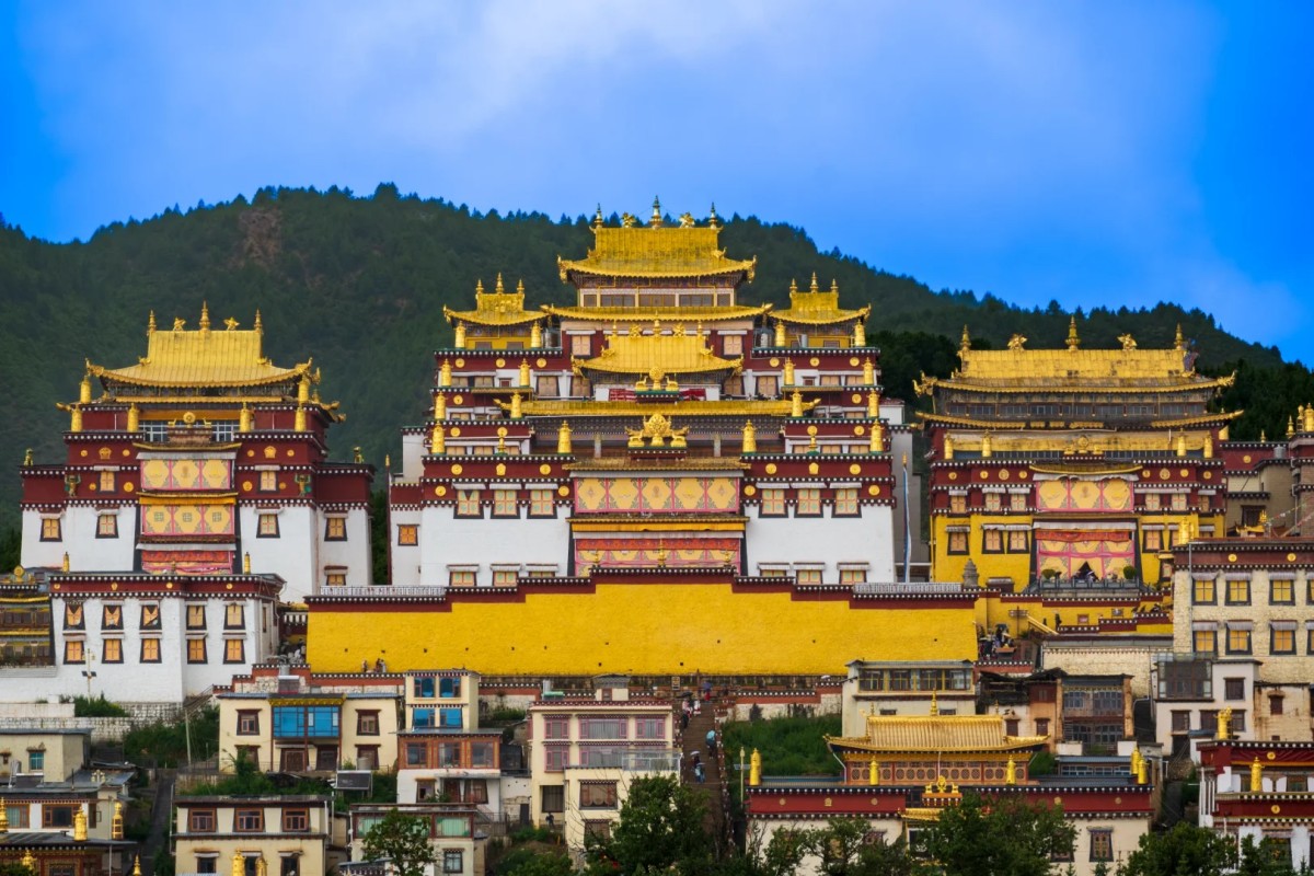 A stunning view of a Tibetan monastery with intricate golden rooftops and vibrant architectural details, set against a lush green mountain backdrop.