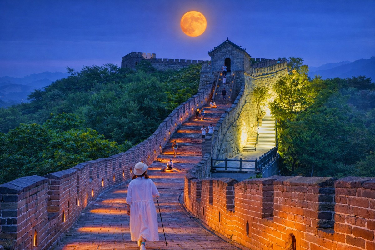 Visitors walking along the illuminated Great Wall at night with a full moon above.