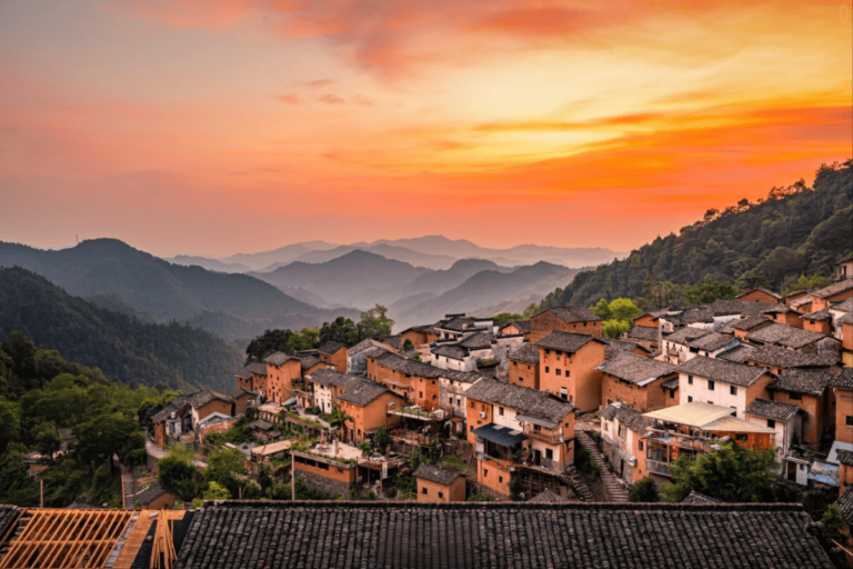 Traditional hillside village with tiled roofs under a colorful sunset sky.