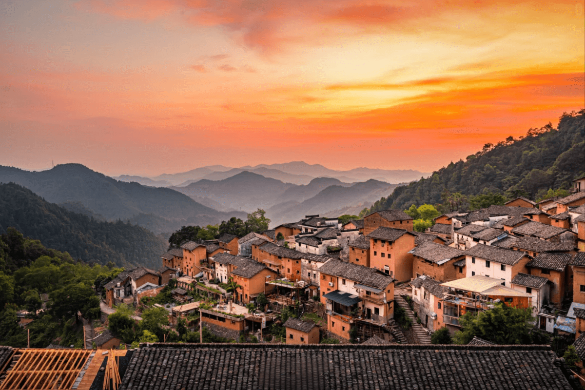 Traditional hillside village with tiled roofs under a colorful sunset sky.