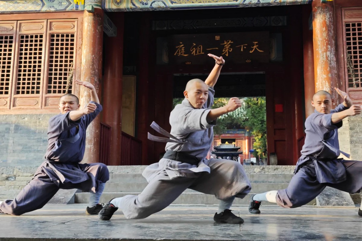 Shaolin monks performing martial arts in front of temple gate.