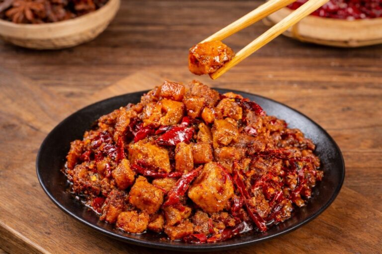 Chopsticks picking spicy Sichuan chicken with dried chilies and peppercorns.