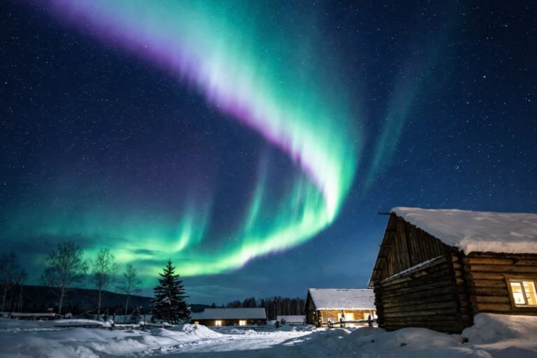 Green and purple northern lights above snowy cabins at night