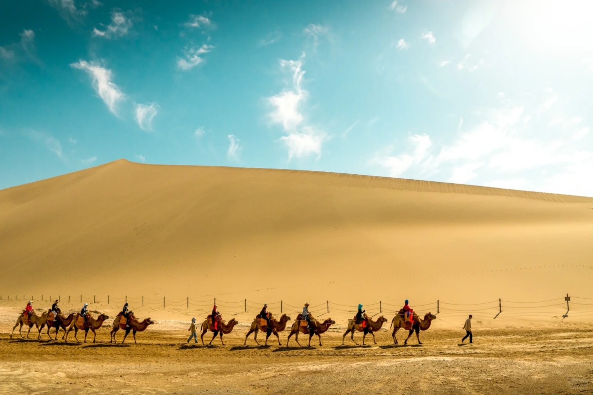 Group traveling by camel along sand dunes in vast desert landscape