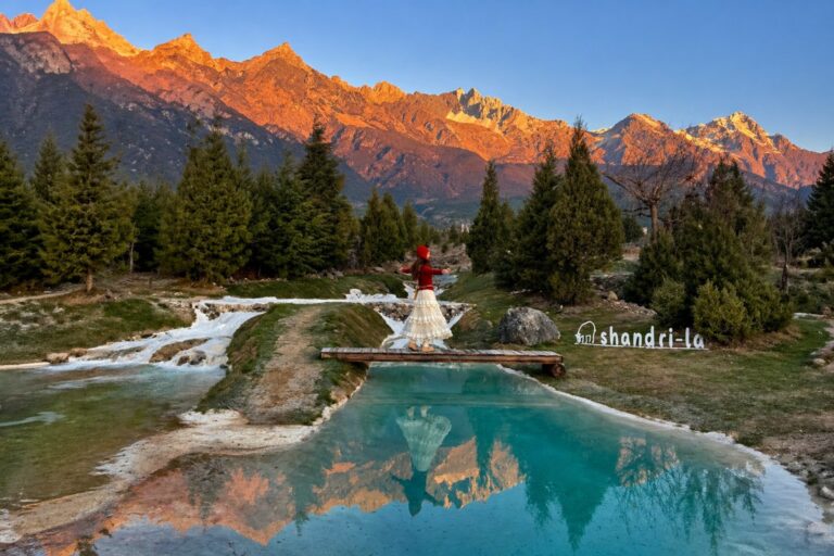 Woman on bridge with snowy mountains reflected in clear water