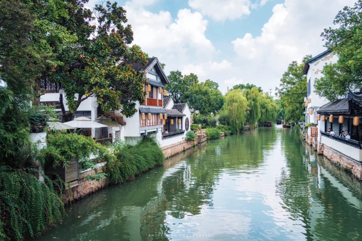 Peaceful canal with white houses, greenery, and boats in Suzhou