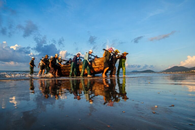 Local fishermen pulling a wooden boat ashore at sunrise on the beach in China