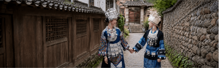 Two women in traditional Chinese ethnic costumes walking through an old village street