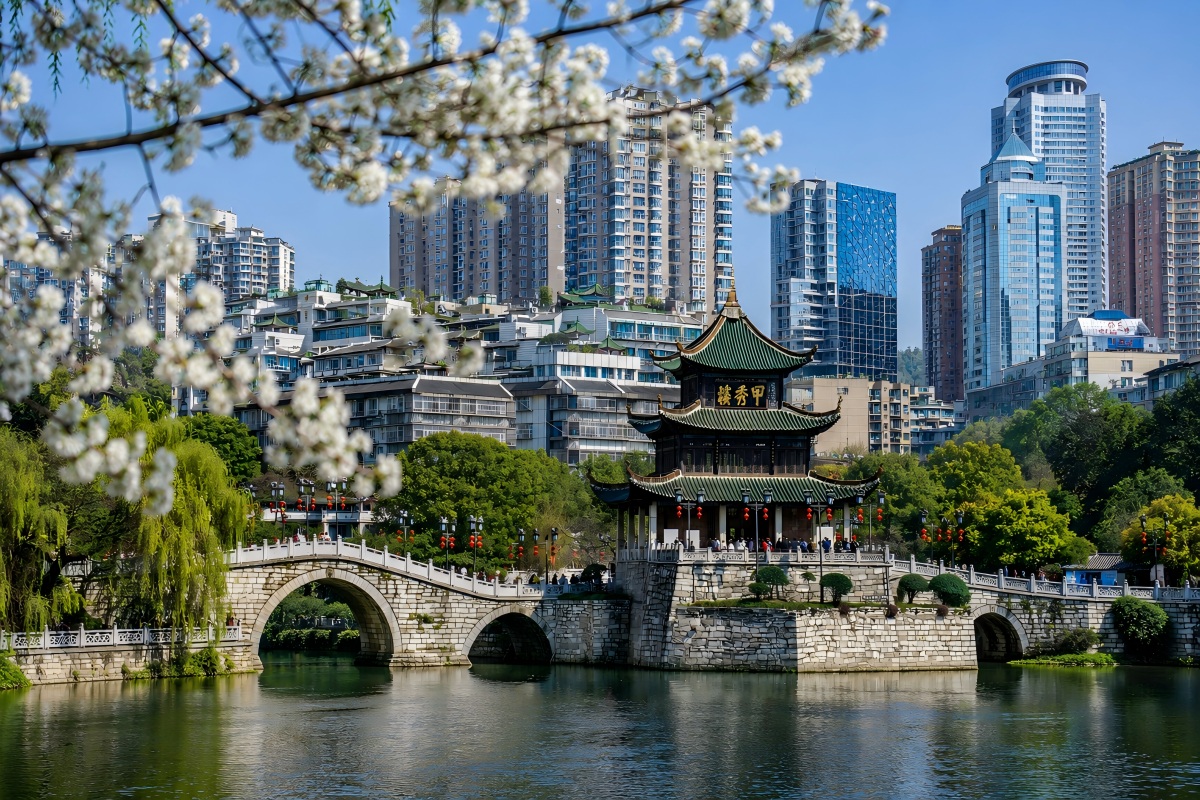Jiaxiu Pavilion by the river with city skyline and spring blossoms in Guiyang