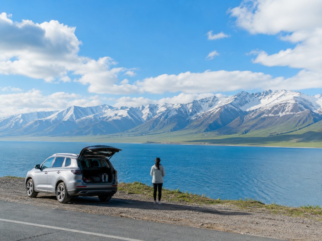 SUV parked by blue lake with snowy mountains and traveler enjoying the view