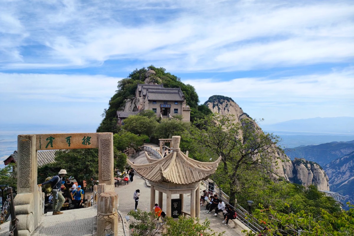 Traditional temple on mountain peak with scenic cliffs and visitors exploring