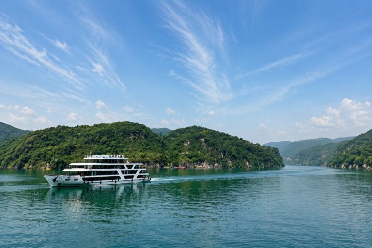 Cruise ship sailing through a peaceful river surrounded by green mountains under blue sky