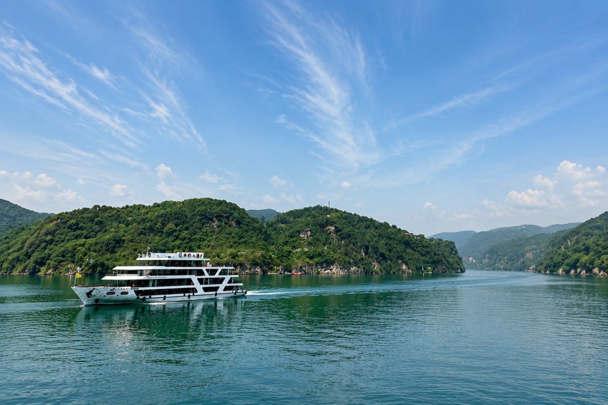 Cruise ship sailing through a peaceful river surrounded by green mountains under blue sky