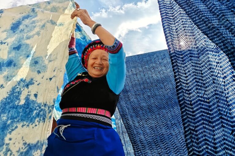Local artisan displaying traditional indigo-dyed fabric in an ethnic village in China