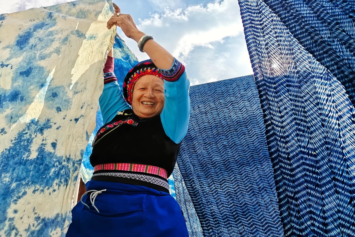 Local artisan displaying traditional indigo-dyed fabric in an ethnic village in China