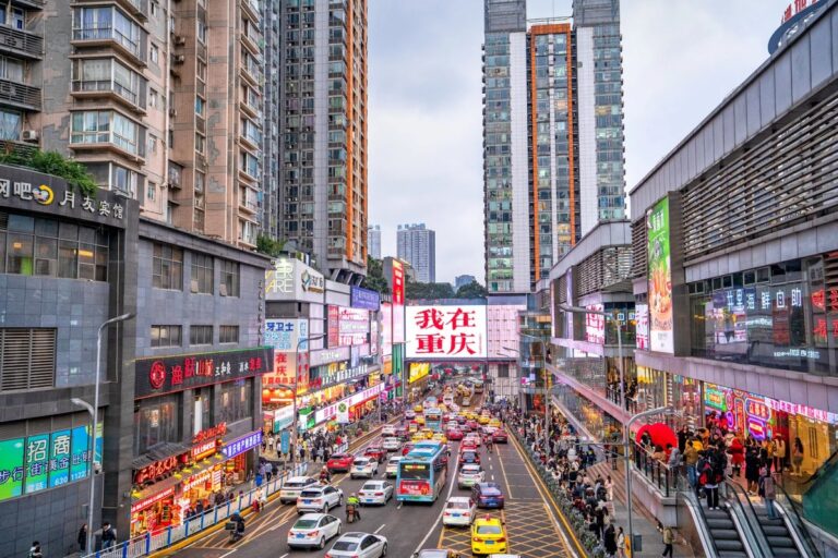 Busy Chongqing shopping street with bright billboards, modern skyscrapers, and lively traffic in the city center.