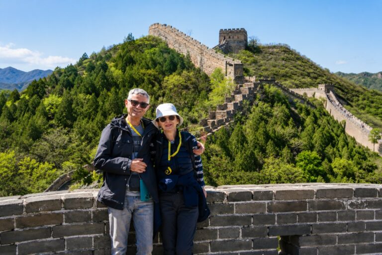 Two travelers posing on the Great Wall with scenic mountain views and historic watchtowers in the background.