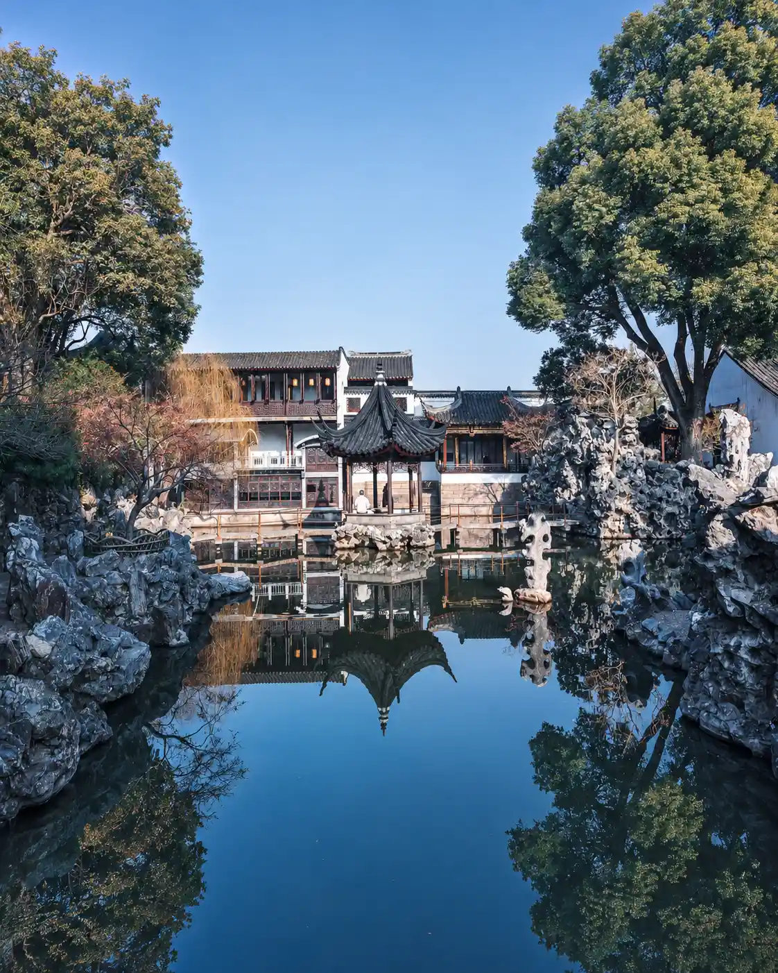 A pavilion in a classical Chinese garden reflected in a pond in winter