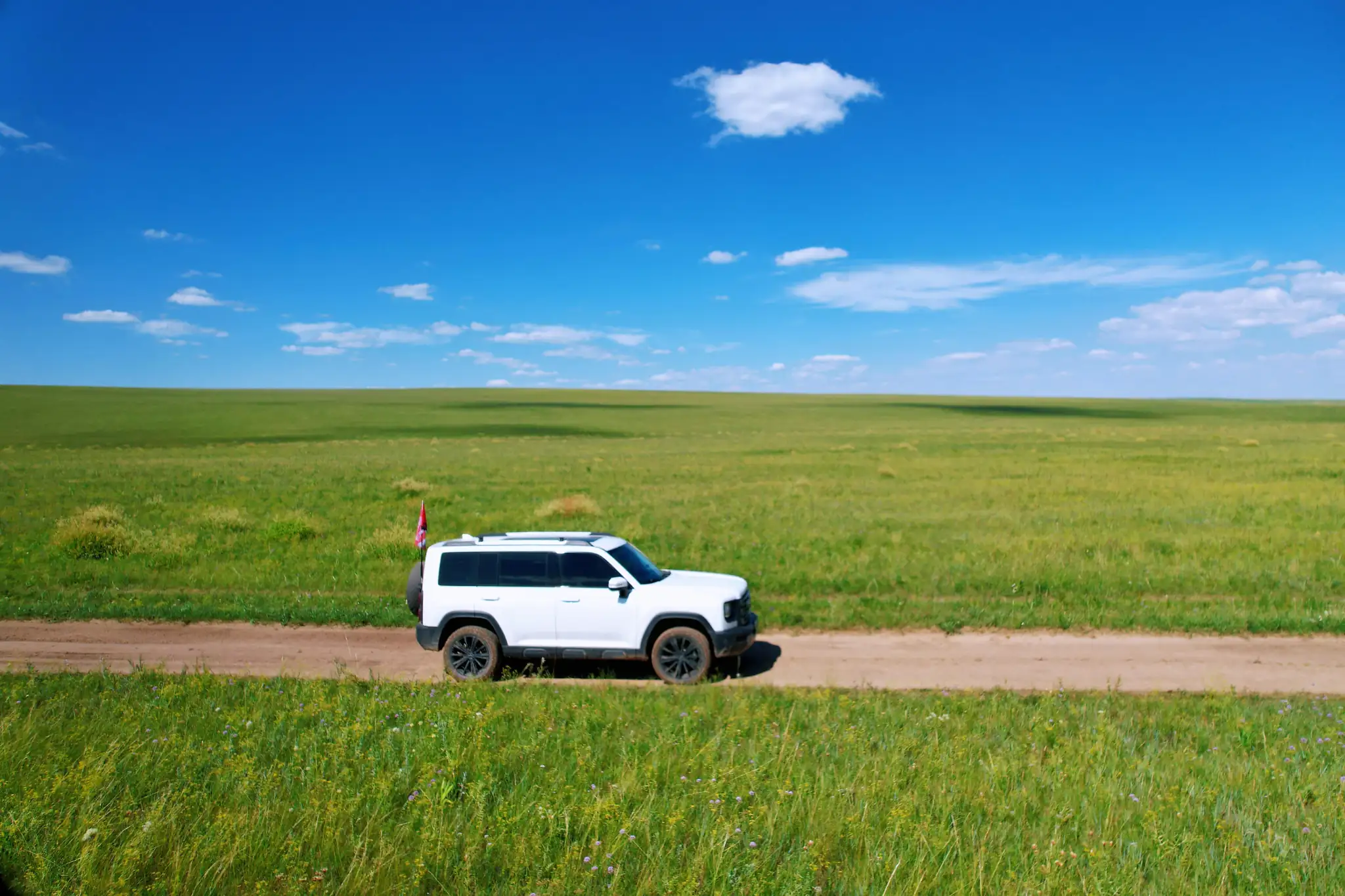 White SUV driving across the vast grasslands of Inner Mongolia